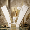 Una lujosa presentación del producto Risala For You Eau de Parfum, con el frasco blanco y dorado de 100 ml y su característico tapón con forma de pluma estilográfica, expuesto dentro de su elegante estuche de regalo con una pluma de ave y un tintero sobre una superficie de mármol.